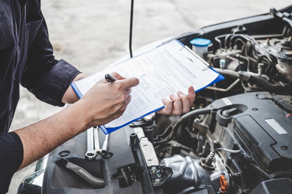 Man with clipboard looking under car hood